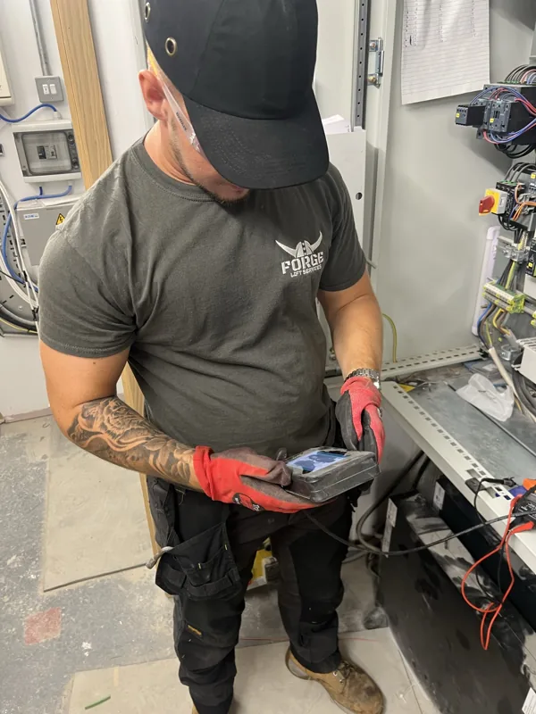 Forge Lifts engineer using an electrical test instrument beside a lift control cabinet